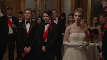 Movie still from “Borat Subsequent Moviefilm” (2020), directed by Jason Woliner – A group of men and women in tuxedos in a room; Medium shot, Over the shoulder angle