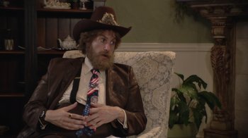 Movie still from “Borat Subsequent Moviefilm” (2020), directed by Jason Woliner – A man in a cowboy hat sitting in a chair; Medium shot, High angle