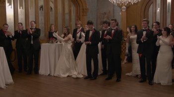 Movie still from “Borat Subsequent Moviefilm” (2020), directed by Jason Woliner – A group of people in formal wear standing in front of a table; Wide shot, Over the shoulder angle