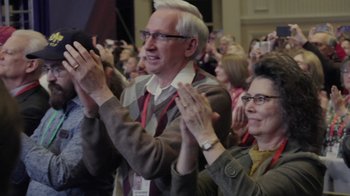 Movie still from “Borat Subsequent Moviefilm” (2020), directed by Jason Woliner – A man and a woman clapping in front of an audience; Medium shot, High angle
