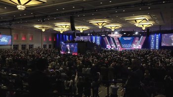 Movie still from “Borat Subsequent Moviefilm” (2020), directed by Jason Woliner – A crowd of people in a room with a microphone; Extreme Wide shot, Low angle