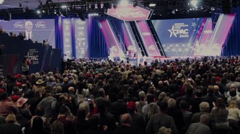 Movie still from “Borat Subsequent Moviefilm” (2020), directed by Jason Woliner – A crowd of people sitting in front of a stage; Extreme Wide shot, High angle