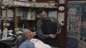Movie still from “Borat Subsequent Moviefilm” (2020), directed by Jason Woliner – A barber cutting a man's hair in a barber shop; Medium shot, Over the shoulder angle