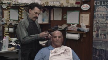 Movie still from “Borat Subsequent Moviefilm” (2020), directed by Jason Woliner – A man getting his hair cut in a barber shop; Medium shot, Over the shoulder angle
