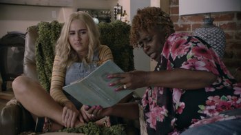 Movie still from “Borat Subsequent Moviefilm” (2020), directed by Jason Woliner – Two women sitting on a couch looking at an open book; Medium shot, Over the shoulder angle