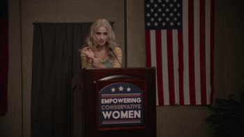 Movie still from “Borat Subsequent Moviefilm” (2020), directed by Jason Woliner – A woman standing at a podium giving a speech; Medium shot, High angle