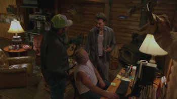 Movie still from “Borat Subsequent Moviefilm” (2020), directed by Jason Woliner – A group of men standing around a table with a computer on it; Wide shot, High angle