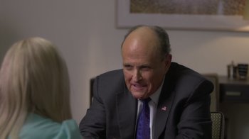 Movie still from “Borat Subsequent Moviefilm” (2020), directed by Jason Woliner – A man in a suit and tie sitting in front of a woman; Close Up shot, Over the shoulder angle