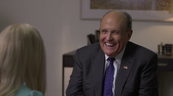 Movie still from “Borat Subsequent Moviefilm” (2020), directed by Jason Woliner – A man in a suit and tie laughing; Close Up shot, Over the shoulder angle