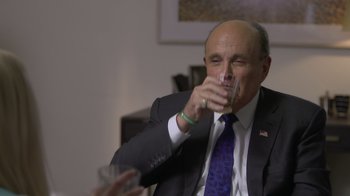 Movie still from “Borat Subsequent Moviefilm” (2020), directed by Jason Woliner – A man in a suit and tie drinking a glass of water; Close Up shot, Over the shoulder angle