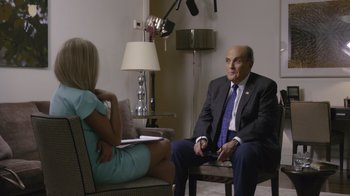 Movie still from “Borat Subsequent Moviefilm” (2020), directed by Jason Woliner – A man in a suit and tie sitting in front of a woman in a blue dress; Medium shot, Over the shoulder angle