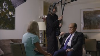 Movie still from “Borat Subsequent Moviefilm” (2020), directed by Jason Woliner – Two men and a woman are sitting in a living room; Medium shot, Over the shoulder angle