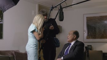 Movie still from “Borat Subsequent Moviefilm” (2020), directed by Jason Woliner – A man in a suit sitting in front of a microphone; Medium shot, Over the shoulder angle