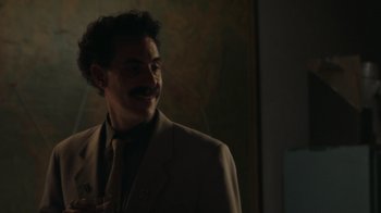 Movie still from “Borat Subsequent Moviefilm” (2020), directed by Jason Woliner – A man in a suit and tie smiling for the camera; Close Up shot, Over the shoulder angle