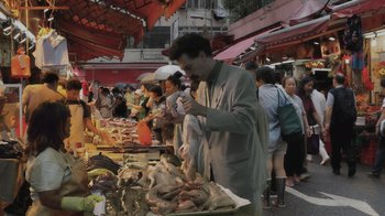 Movie still from “Borat Subsequent Moviefilm” (2020), directed by Jason Woliner – A man standing in front of an outdoor market; Wide shot, High angle