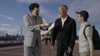 Movie still from “Borat Subsequent Moviefilm” (2020), directed by Jason Woliner – A man in a suit and tie holding a business card next to an older man in a black jacket; Medium shot, Over the shoulder angle