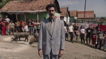 Movie still from “Borat Subsequent Moviefilm” (2020), directed by Jason Woliner – A man in a suit and tie standing in front of a crowd; Wide shot, Over the shoulder angle