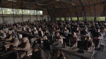 Movie still from “Borat Subsequent Moviefilm” (2020), directed by Jason Woliner – A group of people sitting at tables with laptops; Extreme Wide shot, High angle