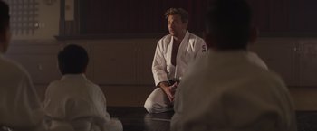 Movie still from “Born a Champion” (2021), directed by Alex Ranarivelo – A man sitting on the ground in a judo uniform; Medium shot, Over the shoulder angle