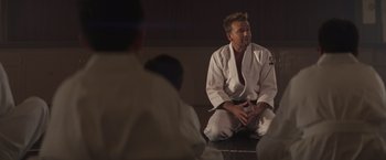 Movie still from “Born a Champion” (2021), directed by Alex Ranarivelo – A man sitting on the ground wearing a white uniform; Close Up shot, Over the shoulder angle
