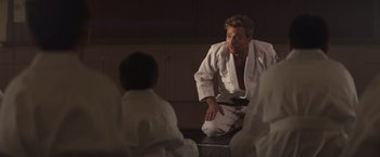Movie still from “Born a Champion” (2021), directed by Alex Ranarivelo – A man sitting on the ground wearing a white uniform; Medium shot, Over the shoulder angle