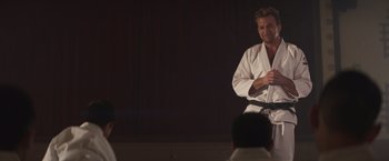 Movie still from “Born a Champion” (2021), directed by Alex Ranarivelo – A man in a white shirt is holding a sword; Medium shot, Over the shoulder angle