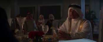 Movie still from “Born a Champion” (2021), directed by Alex Ranarivelo – A man sitting at a table with a glass of wine; Medium shot, Over the shoulder angle