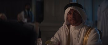 Movie still from “Born a Champion” (2021), directed by Alex Ranarivelo – A man wearing a white shirt and a black hat holding a drink; Close Up shot, Over the shoulder angle