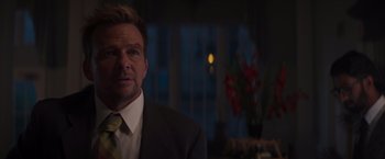 Movie still from “Born a Champion” (2021), directed by Alex Ranarivelo – A man wearing a suit and tie in a dark room; Close Up shot, Over the shoulder angle