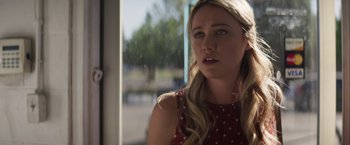 Movie still from “Born a Champion” (2021), directed by Alex Ranarivelo – A young blonde haired woman in a red polka dot dress looking out of a window; Close Up shot, Over the shoulder angle
