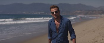 Movie still from “Born a Champion” (2021), directed by Alex Ranarivelo – A man standing on the beach wearing a blue shirt; Medium shot, Over the shoulder angle