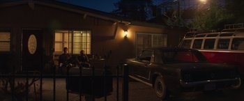 Movie still from “Born a Champion” (2021), directed by Alex Ranarivelo – A man sitting on the back of a car in front of a house at night; Wide shot, Low angle