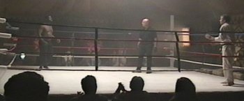 Movie still from “Born a Champion” (2021), directed by Alex Ranarivelo – A man standing in a boxing ring in front of a crowd of onlookers; Wide shot, High angle