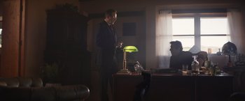 Movie still from “Born a Champion” (2021), directed by Alex Ranarivelo – A man standing in a room with a lamp on a table; Wide shot, Low angle
