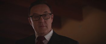 Movie still from “Born a Champion” (2021), directed by Alex Ranarivelo – A person wearing glasses and a suit; Close Up shot, Low angle