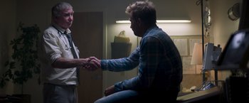 Movie still from “Born a Champion” (2021), directed by Alex Ranarivelo – Two men shaking hands in a room; Medium shot, Over the shoulder angle