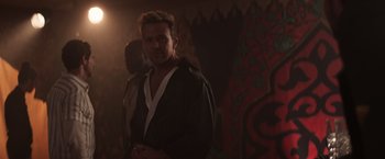 Movie still from “Born a Champion” (2021), directed by Alex Ranarivelo – A man standing in a dark room wearing a bathrobe; Medium shot, Over the shoulder angle