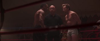 Movie still from “Born a Champion” (2021), directed by Alex Ranarivelo – Three men standing in a boxing ring talking to a referee; Medium shot, Over the shoulder angle
