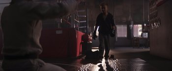Movie still from “Born a Champion” (2021), directed by Alex Ranarivelo – A man is walking in a dark room with luggage; Wide shot, Over the shoulder angle