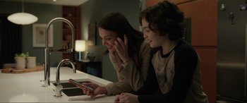 Movie still from “Brahms: The Boy II” (2020), directed by William Brent Bell – Two people sitting at a table looking at a phone; Medium shot, Over the shoulder angle