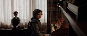 A boy sitting in front of a piano in a living room