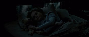 Movie still from “Brahms: The Boy II” (2020), directed by William Brent Bell – A woman laying in bed with a teddy bear; Close Up shot, High angle