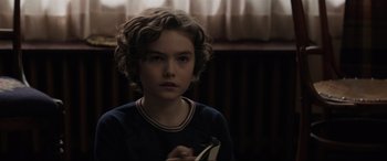 Movie still from “Brahms: The Boy II” (2020), directed by William Brent Bell – A young boy with curly hair is holding a book; Close Up shot, Over the shoulder angle