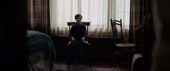 Movie still from “Brahms: The Boy II” (2020), directed by William Brent Bell – A doll sitting on a chair in a room; Wide shot, Over the shoulder angle
