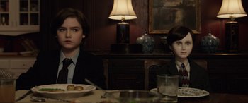 Movie still from “Brahms: The Boy II” (2020), directed by William Brent Bell – Two people sitting at a dinner table with plates of food in front of them; Medium shot, Over the shoulder angle