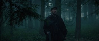 Movie still from “Brahms: The Boy II” (2020), directed by William Brent Bell – A man standing in the middle of a forest holding a gun; Medium shot, Low angle