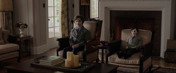 Movie still from “Brahms: The Boy II” (2020), directed by William Brent Bell – A young boy sitting in a chair in a living room; Wide shot, Over the shoulder angle