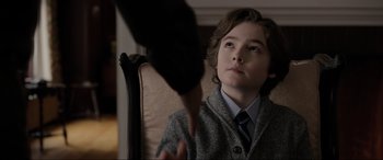 Movie still from “Brahms: The Boy II” (2020), directed by William Brent Bell – A young boy sitting in a chair with a hand reaching toward him; Close Up shot, Over the shoulder angle
