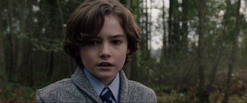 Movie still from “Brahms: The Boy II” (2020), directed by William Brent Bell – A boy in a suit and tie in a wooded area; Close Up shot, Over the shoulder angle