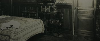 Movie still from “Brahms: The Boy II” (2020), directed by William Brent Bell – An old photo of a boy sitting in a chair in front of a bed; Wide shot, High angle
